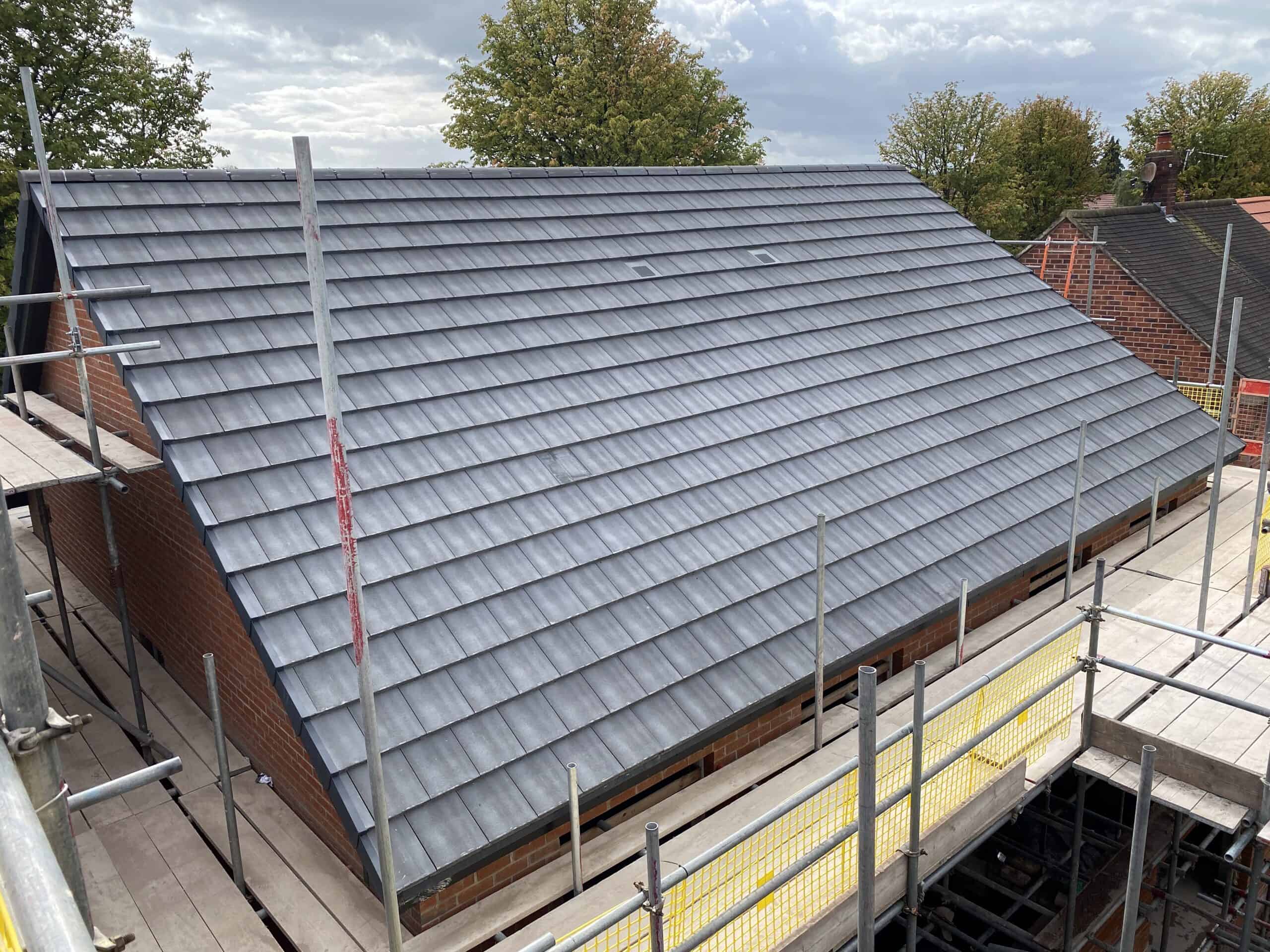 A newly constructed, large gray tiled roof on a building surrounded by scaffolding. The scene is set outdoors under a partly cloudy sky, with trees in the background.